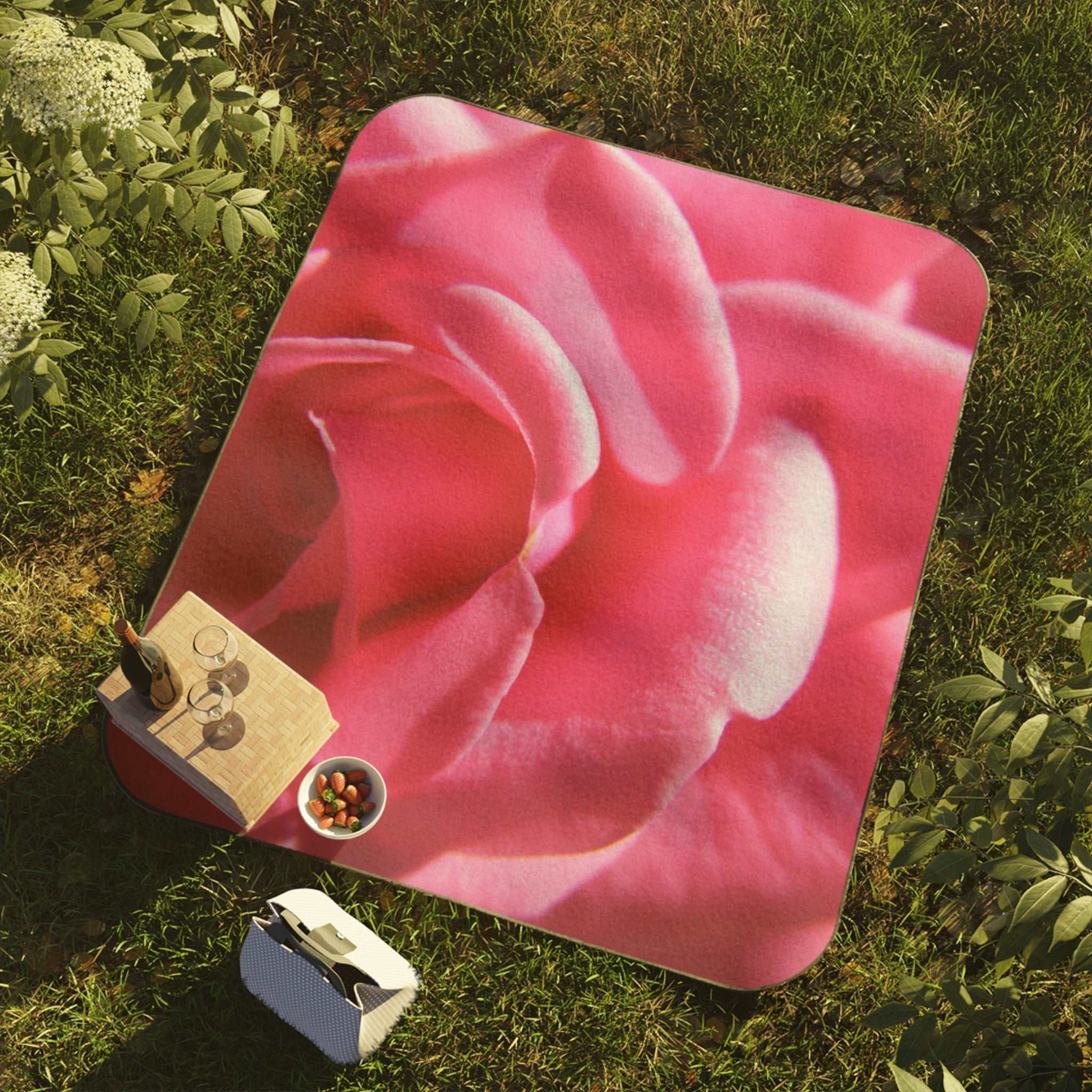 Pink Rose Picnic Blanket Pink floral mat on grass with a small bag and container.