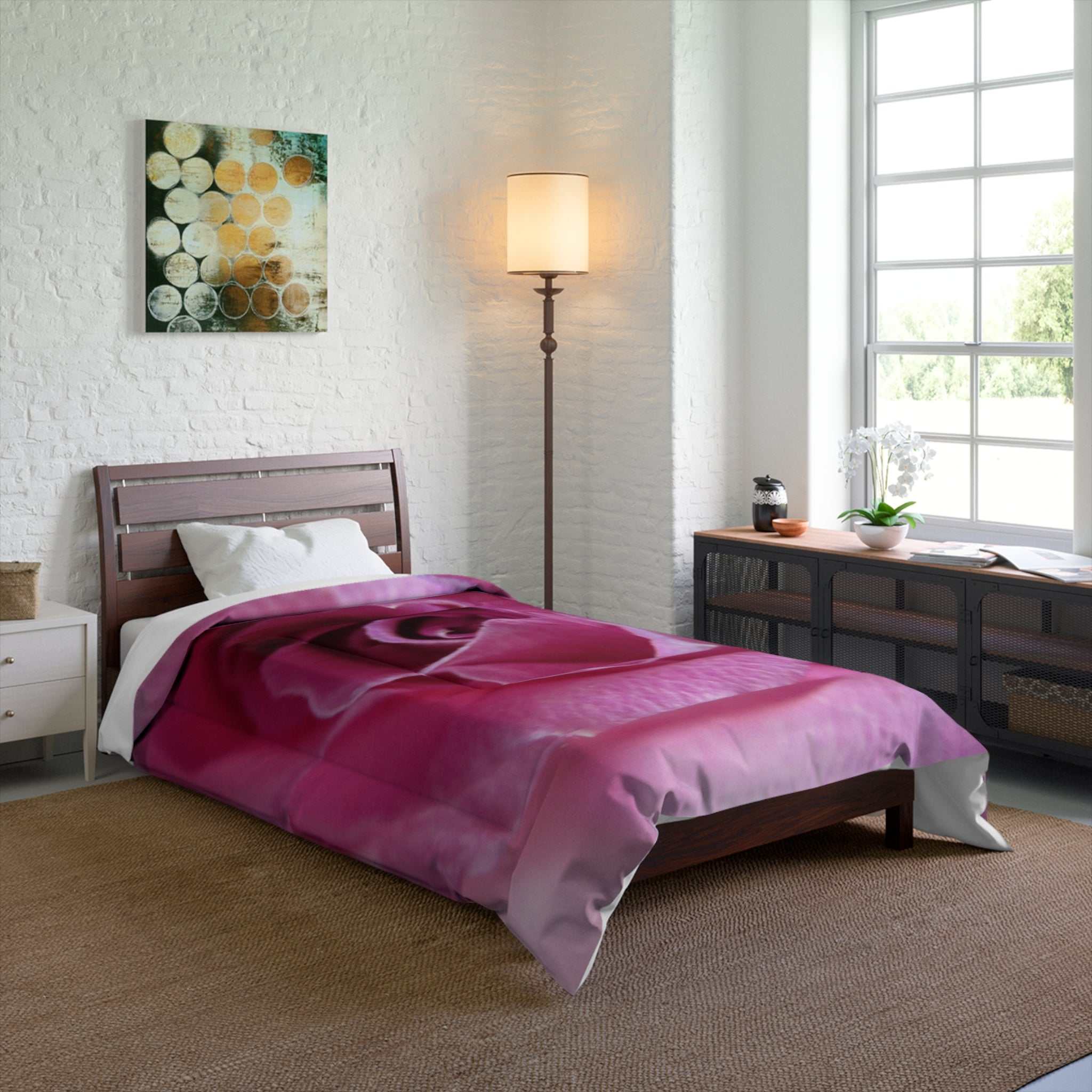 Bedroom with a bed covered in a pink comforter, lamp, and artwork on the wall.