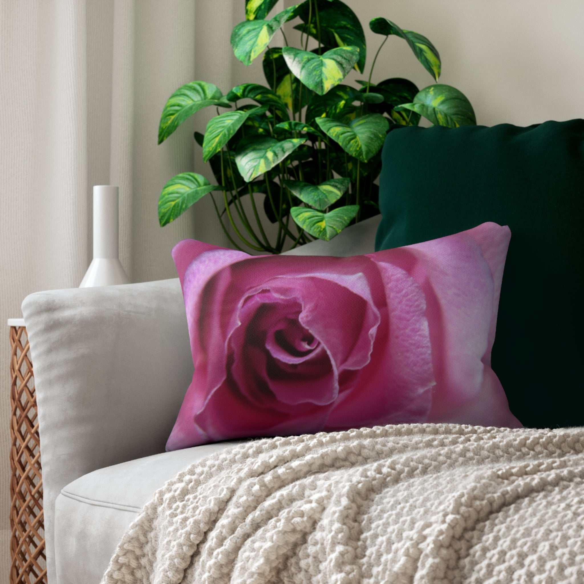 Pink rose pillow on a couch with a plant in the background